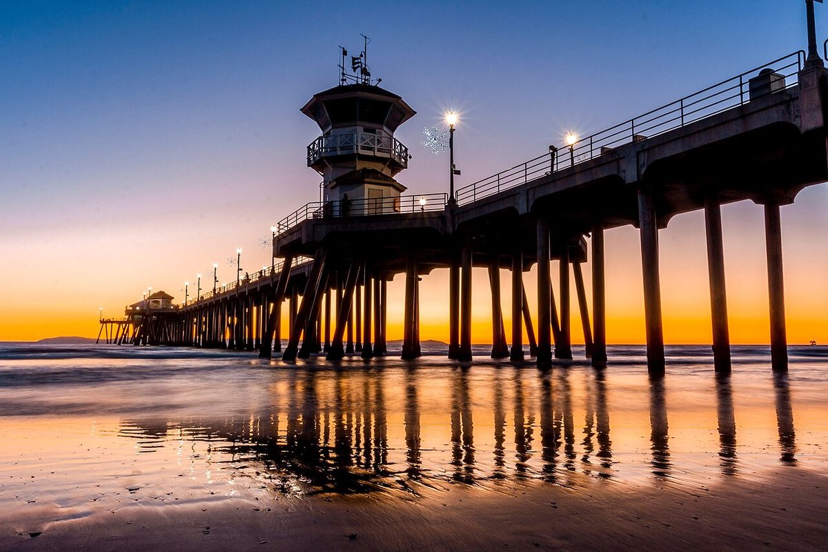 Huntington Beach Pier at sunset with its reflection on the wet sand in Huntington Beach, California